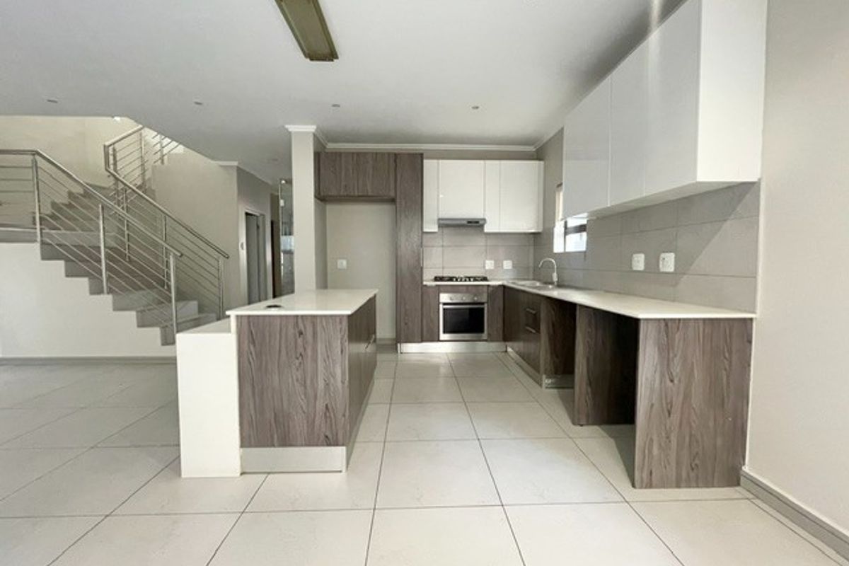 Modern open-plan kitchen featuring two-tone cabinetry, a central island, built-in oven, and sleek tiled flooring, adjacent to a staircase with stainless steel railings.