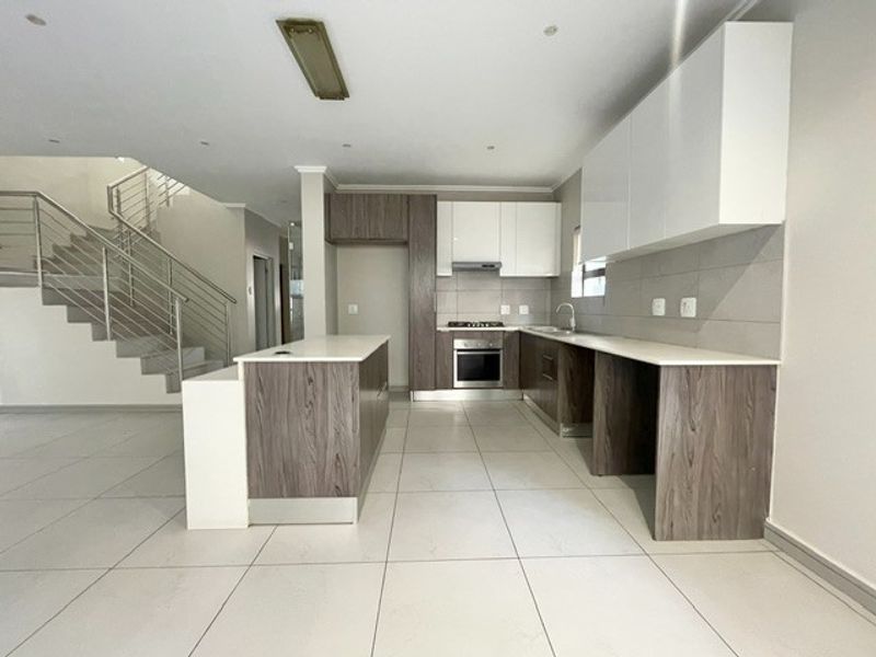 Modern open-plan kitchen featuring two-tone cabinetry, a central island, built-in oven, and sleek tiled flooring, adjacent to a staircase with stainless steel railings.