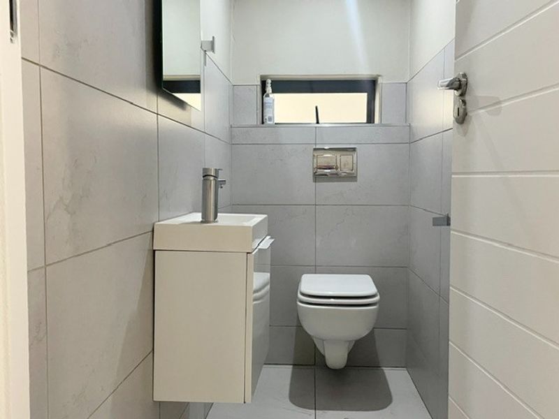 A modern, compact guest bathroom featuring a wall-mounted toilet with a concealed cistern, a sleek vanity basin, and neutral floor-to-ceiling tiling.