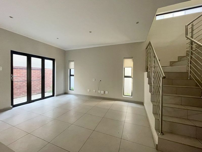 Spacious, light-filled living area featuring neutral tiled flooring, a modern staircase with stainless steel balustrades, and bi-fold doors leading to the exterior.