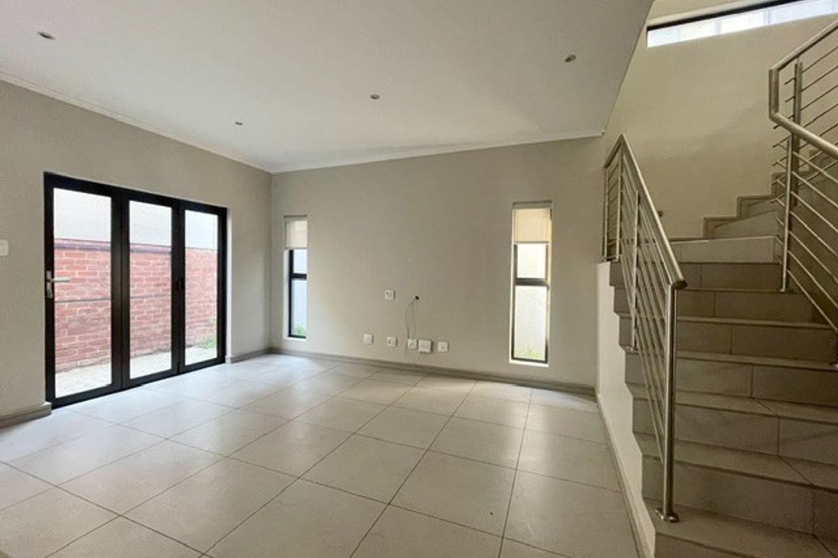 Spacious, light-filled living area featuring neutral tiled flooring, a modern staircase with stainless steel balustrades, and bi-fold doors leading to the exterior.