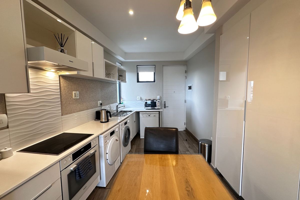 Modern galley-style kitchen featuring sleek white cabinetry, integrated appliances, a textured splashback, and recessed lighting, offering a clean and functional cooking space.