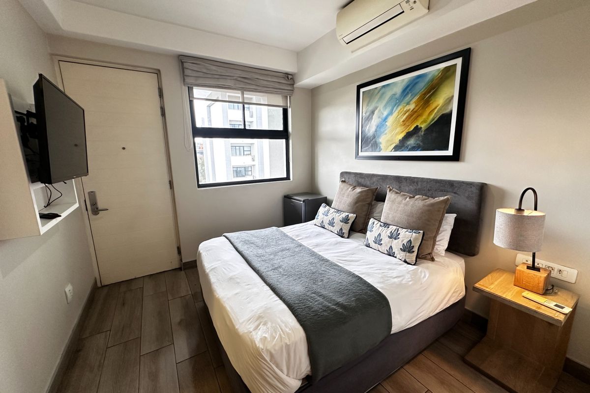 A well-maintained bedroom featuring tiled flooring, a wall-mounted air conditioning unit, and a window with a roller blind.
