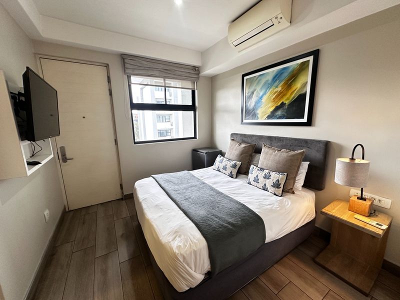 A well-maintained bedroom featuring tiled flooring, a wall-mounted air conditioning unit, and a window with a roller blind.