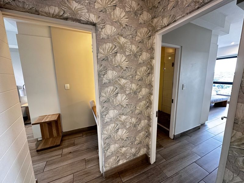A well-maintained hallway featuring modern wood-look floor tiles and decorative wallpaper, providing access to adjacent rooms within the apartment.
