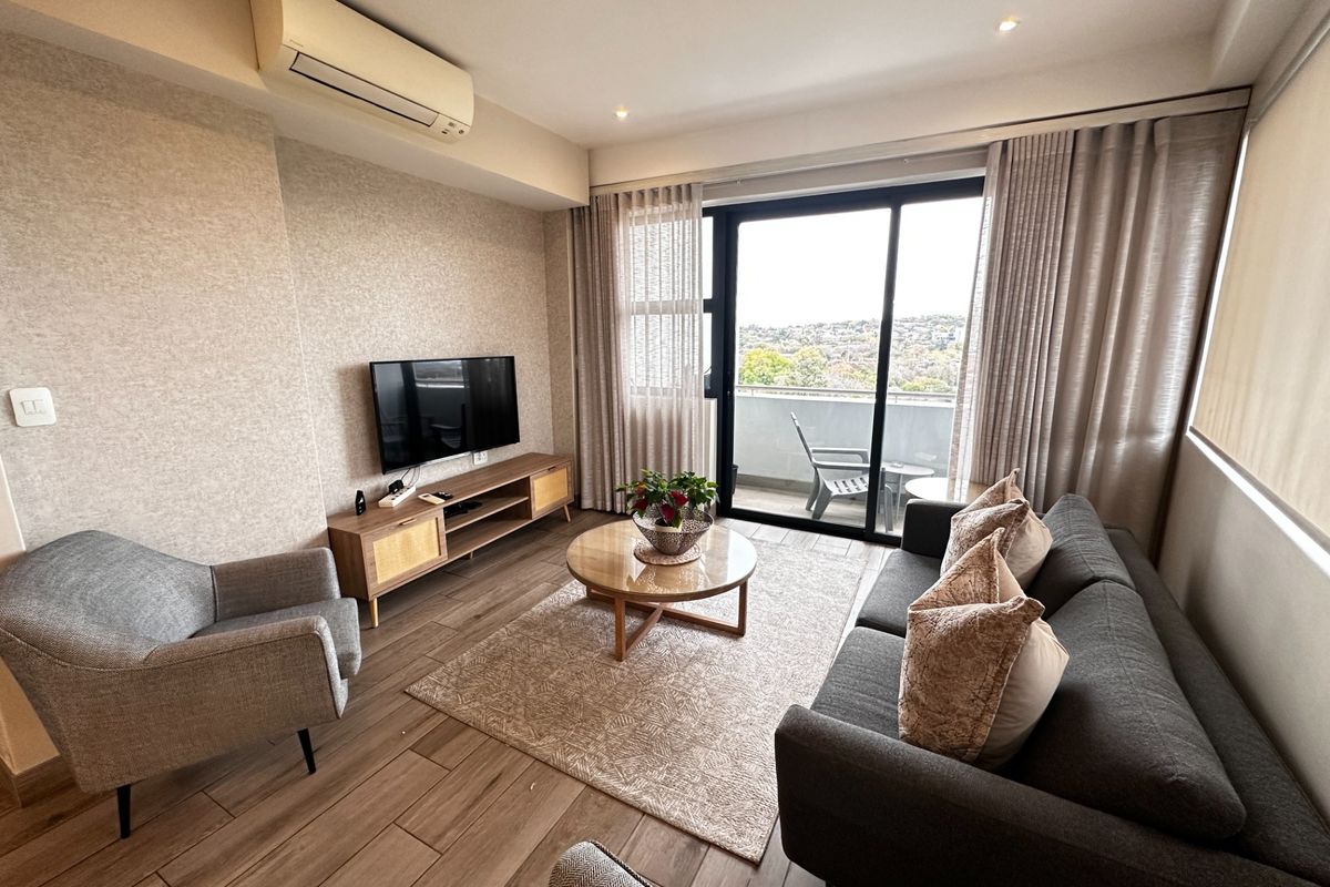 A well-maintained living room featuring wood-look tile flooring, a wall-mounted air conditioner, and large sliding glass doors leading to a private balcony.
