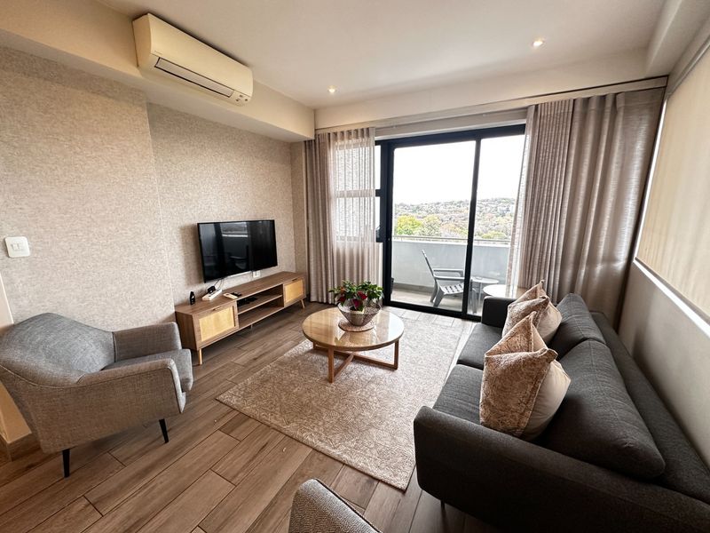 A well-maintained living room featuring wood-look tile flooring, a wall-mounted air conditioner, and large sliding glass doors leading to a private balcony.