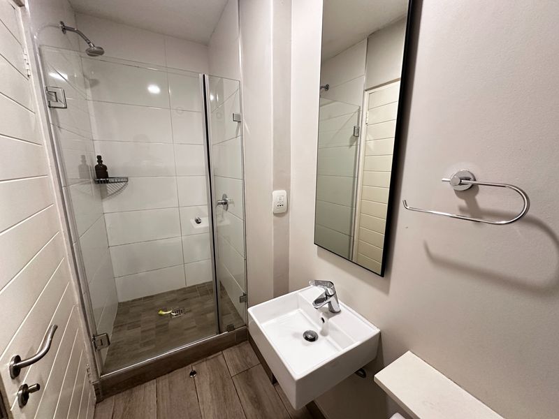 A modern, compact bathroom featuring a glass-enclosed shower, wall-mounted basin with chrome fixtures, and a sleek mirror.
