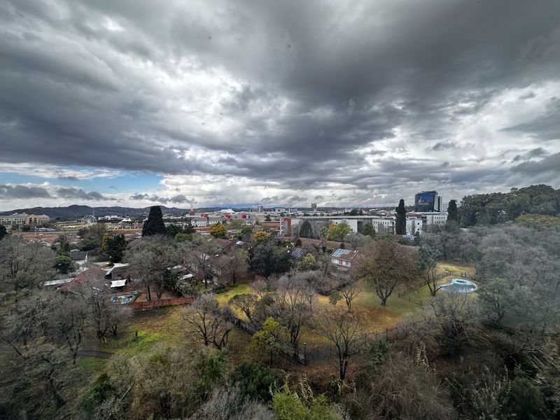 An elevated panoramic view overlooking a suburban landscape with mature trees, residential properties, and a distant cityscape under a cloudy sky.