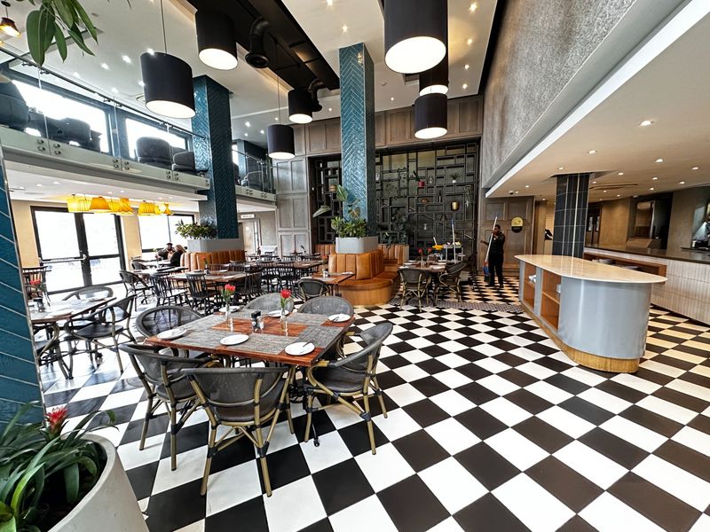 Spacious open-plan dining area featuring high ceilings, a mezzanine level, distinctive checkered flooring, and modern built-in service counters and booth seating.