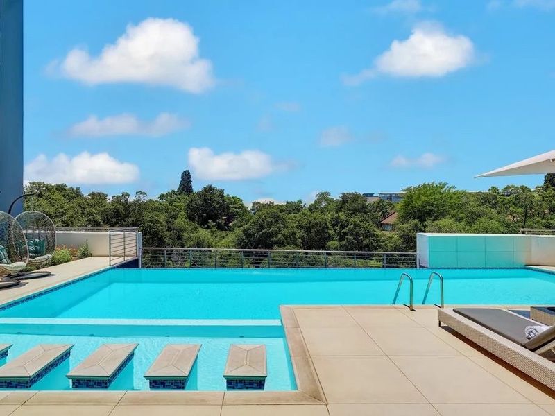 A well-maintained outdoor swimming pool area featuring a tiled deck, metal safety railings, and clear views of the surrounding landscape.