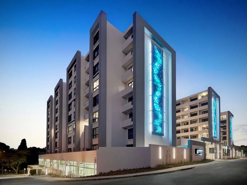 A modern apartment building exterior at dusk, featuring contemporary architectural design, illuminated decorative panels, and clean, well-maintained structural finishes.