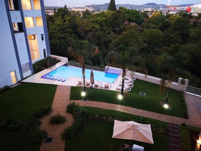 Elevated view of a well-maintained apartment complex pool area featuring a swimming pool, landscaped gardens, and paved pathways.
