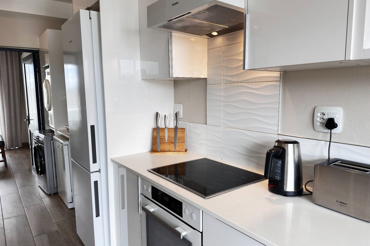 Modern kitchen featuring high-gloss cabinetry, integrated appliances, electric hob with extractor fan, and a textured tiled backsplash.