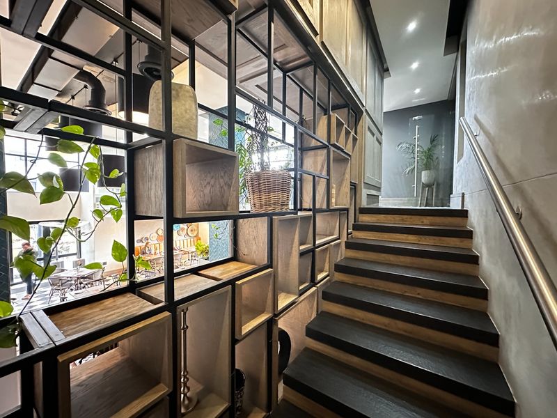 A modern staircase featuring a custom metal and timber shelving partition, recessed lighting, and a sleek stainless steel handrail.