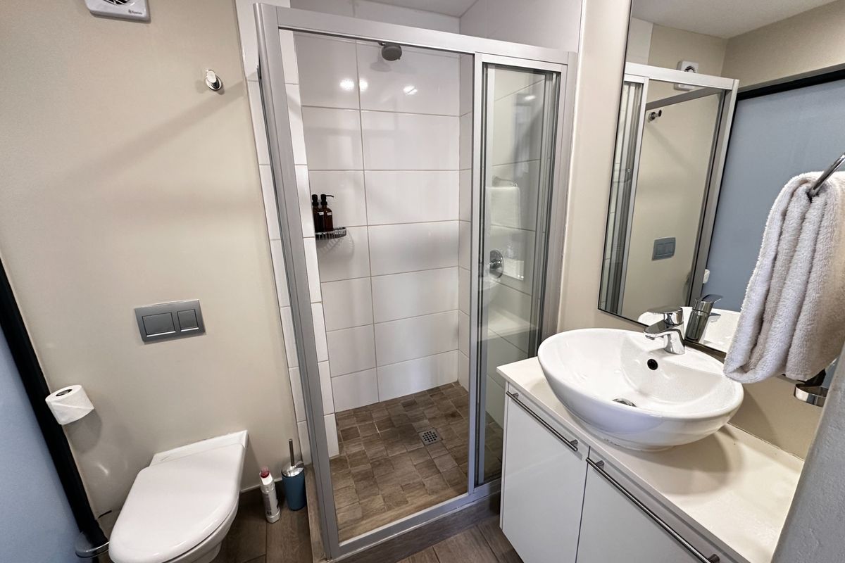 Modern bathroom featuring a glass-enclosed shower, wall-mounted toilet, and a sleek vanity with a vessel sink and large mirror.