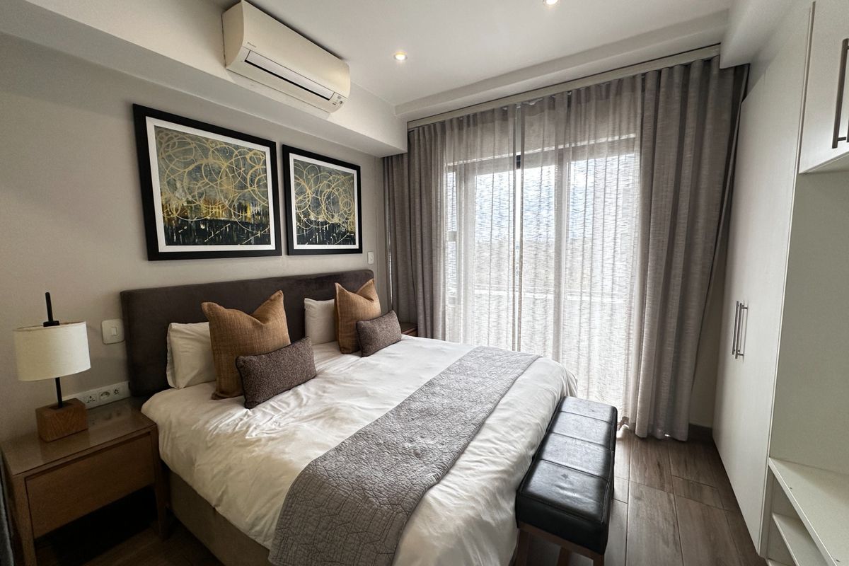 A well-maintained bedroom featuring tiled flooring, built-in cupboards, a split-system air conditioner, and a sliding glass door providing natural light.