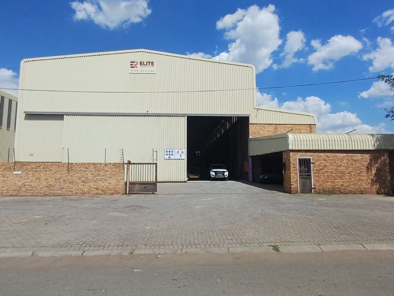 Front elevation of an industrial warehouse featuring corrugated metal cladding, a paved driveway, and secure perimeter brick walling with electric fencing.