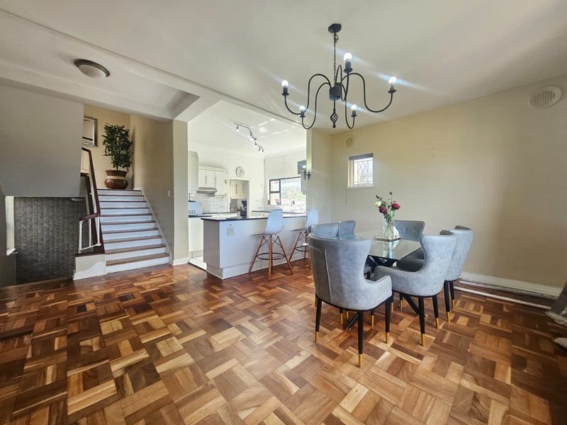 Open-plan dining area featuring classic parquet flooring and a staircase, flowing into a functional kitchen with built-in cabinetry and island seating.