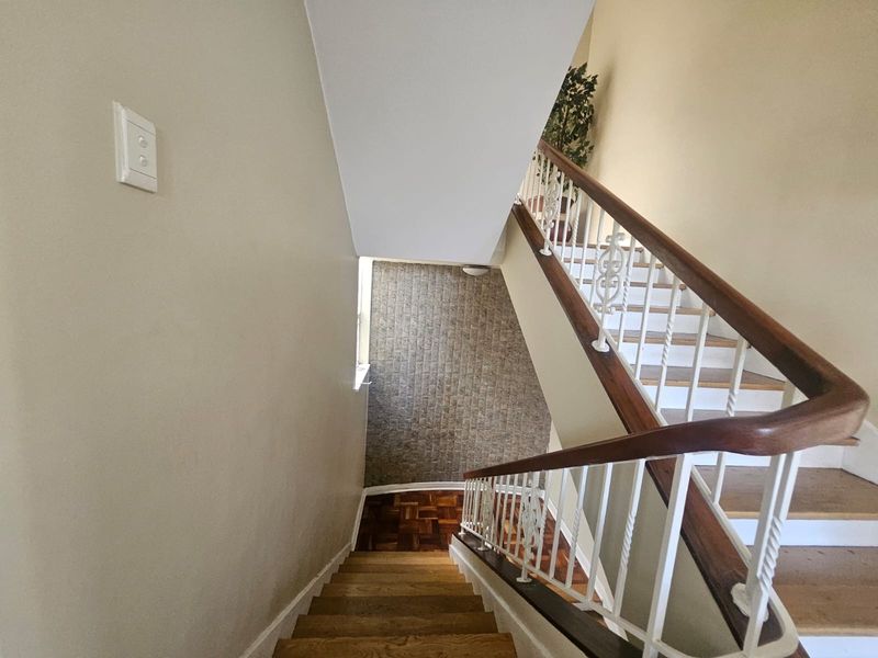 A staircase featuring wooden treads, a classic wrought iron balustrade with a wooden handrail, and parquet flooring at the landing.