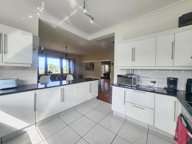 Open-plan kitchen featuring white cabinetry, black granite countertops, and subway tile backsplash, flowing into the adjacent living area with views.