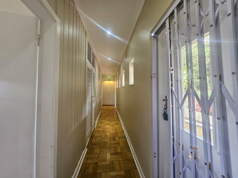 A well-lit hallway featuring parquet flooring, built-in storage cupboards, and a secure metal gate leading to the exterior.