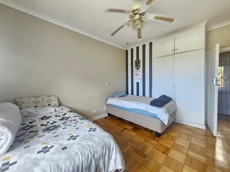 A bedroom featuring parquet flooring, built-in cupboards, and a ceiling fan, offering a functional space with classic finishes.