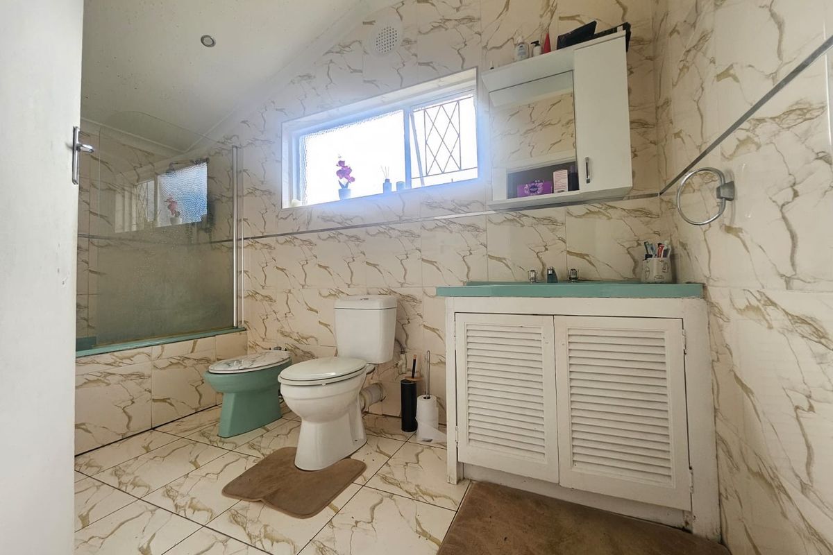 A dated bathroom featuring marble-look wall and floor tiles, a built-in vanity, toilet, and a bathtub with a glass shower screen.
