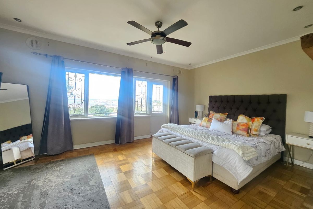Spacious bedroom featuring classic parquet flooring, a ceiling fan, and large windows with security bars, offering natural light and elevated views.