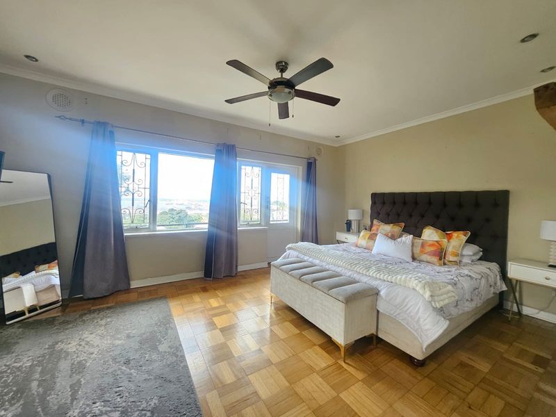 Spacious bedroom featuring classic parquet flooring, a ceiling fan, and large windows with security bars, offering natural light and elevated views.