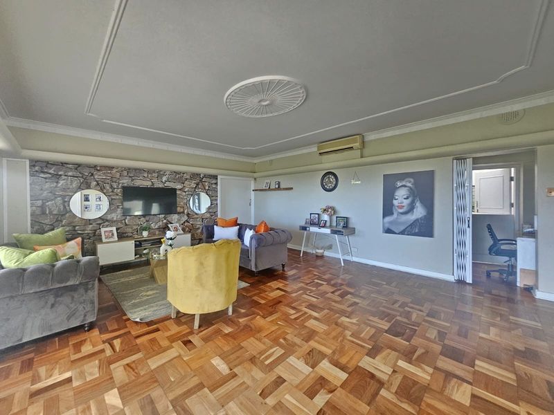 Spacious living room featuring classic parquet flooring, a decorative stone feature wall, and elegant ceiling detailing with integrated air conditioning.