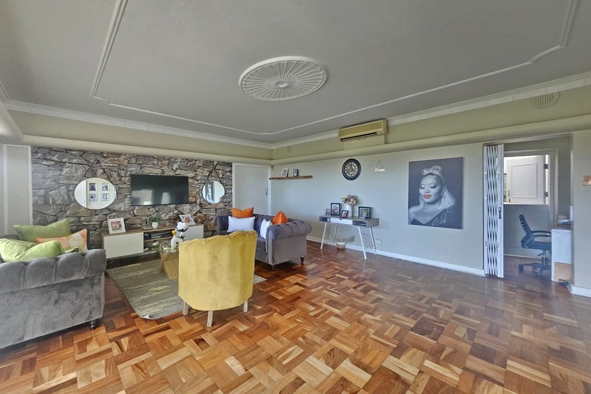 Spacious living room featuring classic parquet flooring, a decorative stone feature wall, and elegant ceiling detailing with integrated air conditioning.