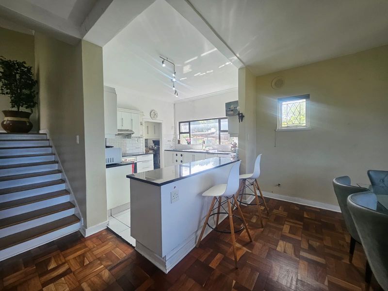 Open-plan kitchen and dining area featuring a central island with granite countertop, parquet flooring, and direct access to the staircase.