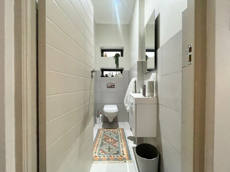 A modern, compact guest bathroom featuring a wall-mounted vanity, wall-hung toilet, and neutral tiled finishes.