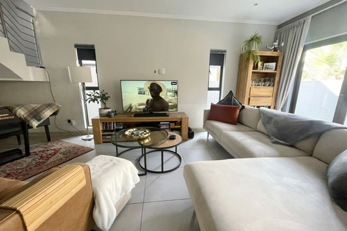 A bright and modern living room featuring large format floor tiles, recessed lighting, and a staircase with a contemporary metal railing.
