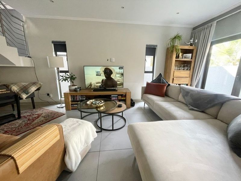 A bright and modern living room featuring large format floor tiles, recessed lighting, and a staircase with a contemporary metal railing.