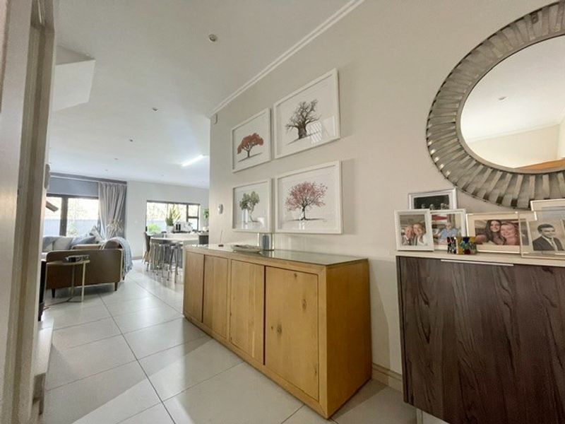 A bright and well-maintained hallway featuring neutral tiled flooring and recessed downlighting, leading into an open-plan living and kitchen area.