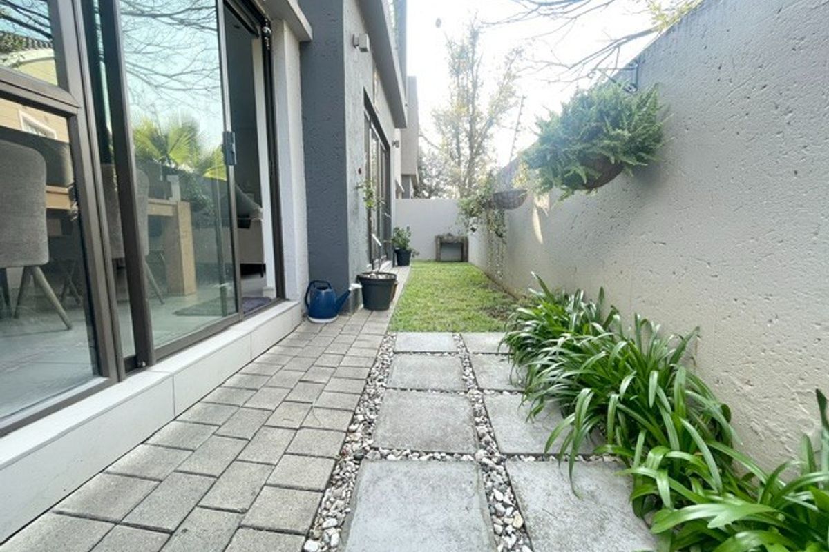 A side garden area featuring a paved walkway, a small lawn, and large sliding glass doors providing access to the interior living space.