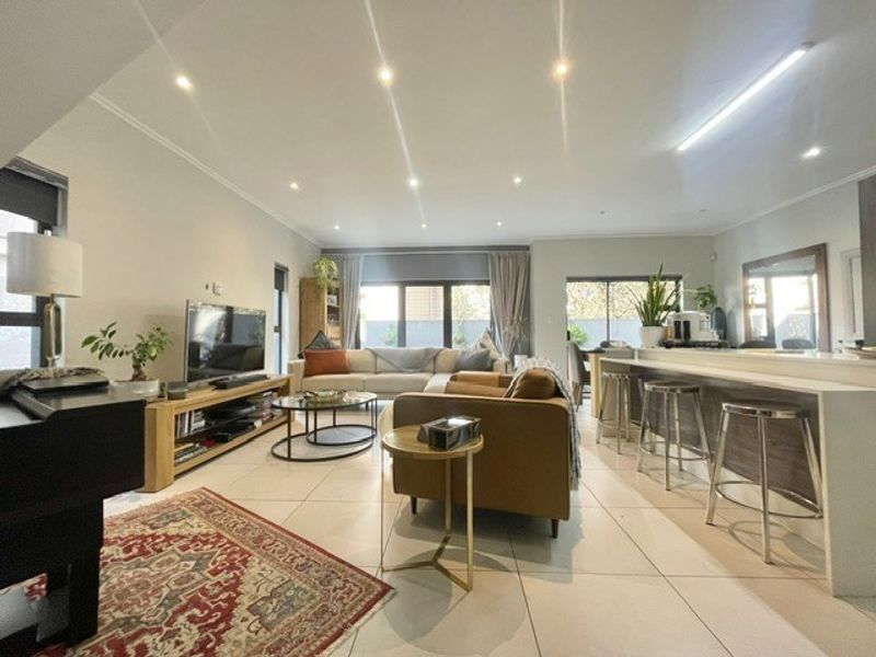 Spacious open-plan living area featuring tiled flooring, recessed downlighting, and a functional kitchen breakfast bar with seamless flow to the outdoor space.