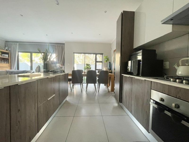 Modern open-plan kitchen and dining area featuring contemporary wood-finish cabinetry, stone countertops, integrated appliances, and large sliding doors leading to the outdoor space.