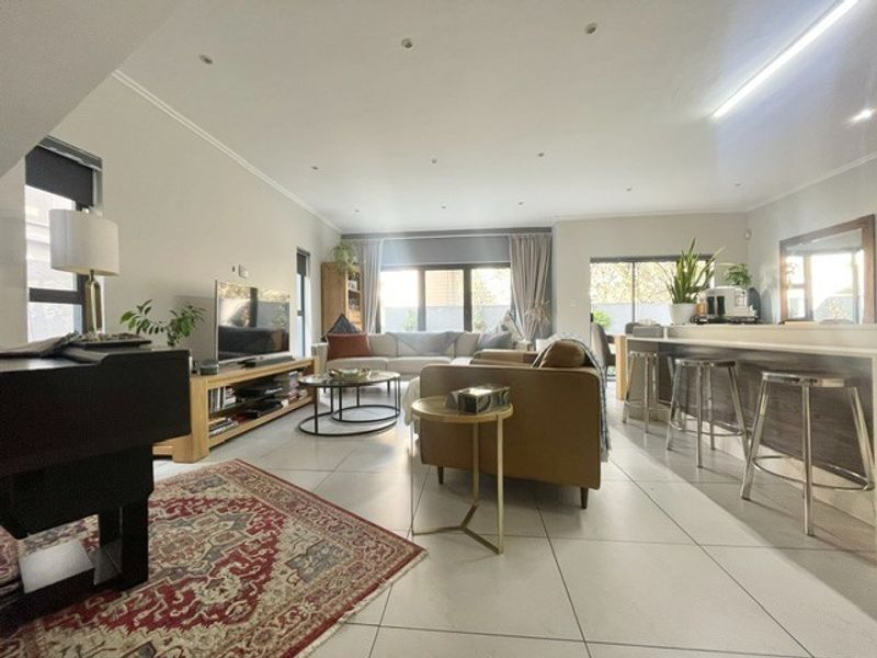 Spacious open-plan living area featuring large format floor tiles, recessed lighting, and a functional kitchen island with breakfast bar seating.