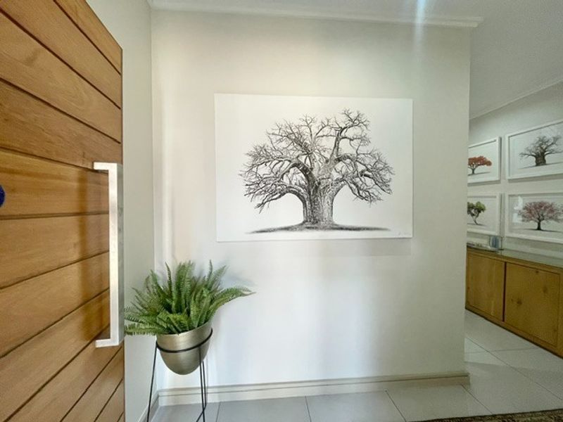 A bright and welcoming entrance hall featuring a modern timber pivot door, neutral walls, and clean tiled flooring.