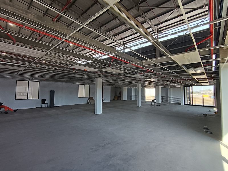 Spacious open-plan industrial unit featuring exposed ceiling grid, fire sprinkler system, concrete flooring, and large windows providing ample natural light.