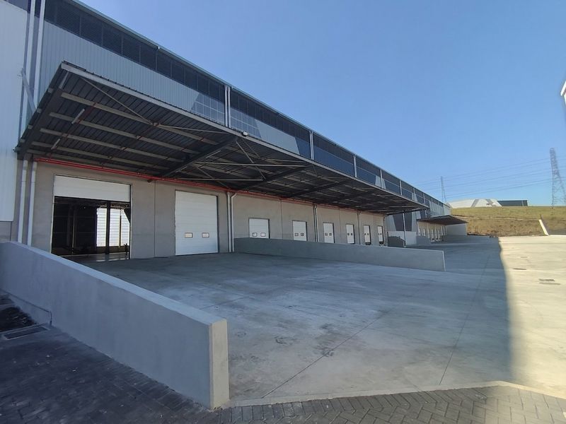 Industrial warehouse exterior featuring multiple loading bays with roller shutter doors, a large concrete loading apron, and an extensive overhead steel canopy.