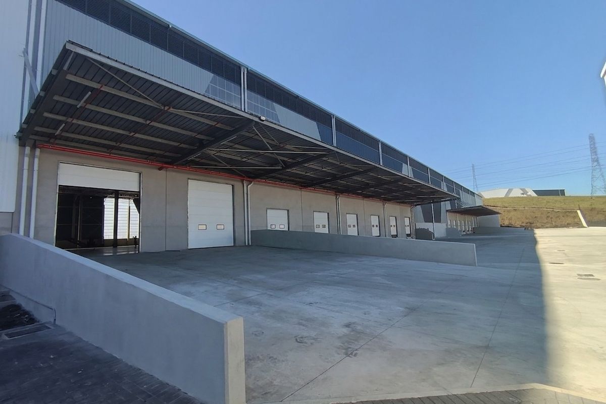Industrial warehouse exterior featuring multiple loading bays with roller shutter doors, a large concrete loading apron, and an extensive overhead steel canopy.