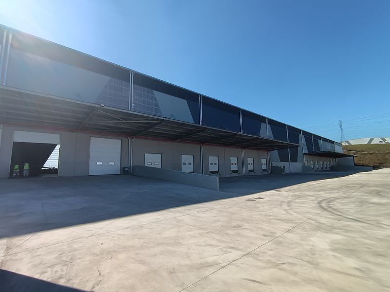 Industrial warehouse exterior featuring multiple loading docks, roller shutter doors, and a large concrete yard area under a steel canopy.