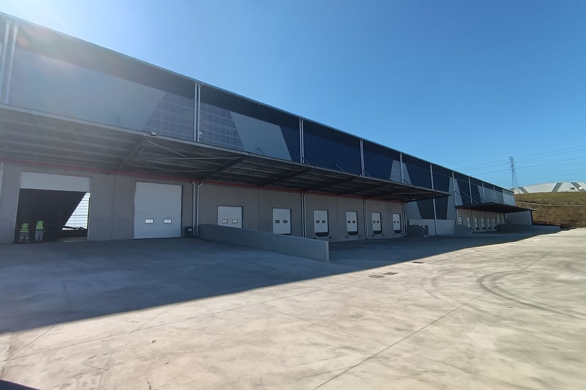 Industrial warehouse exterior featuring multiple loading docks, roller shutter doors, and a large concrete yard area under a steel canopy.