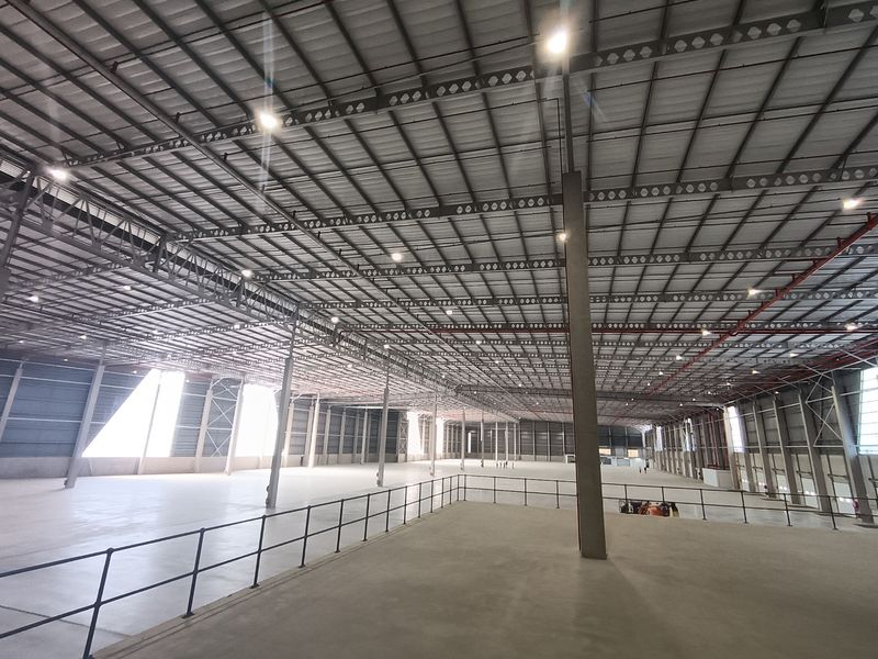 Expansive industrial warehouse space featuring a high-clearance steel portal frame, polished concrete flooring, integrated fire sprinkler system, and a mezzanine level with safety railing.