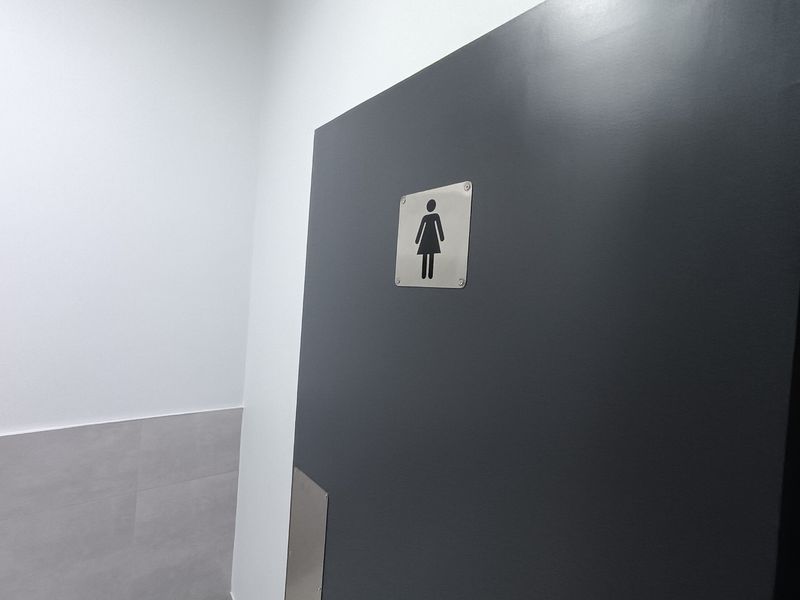 A clean, modern industrial restroom facility featuring a clearly marked female entrance with neutral wall finishes and tiled lower wall sections.