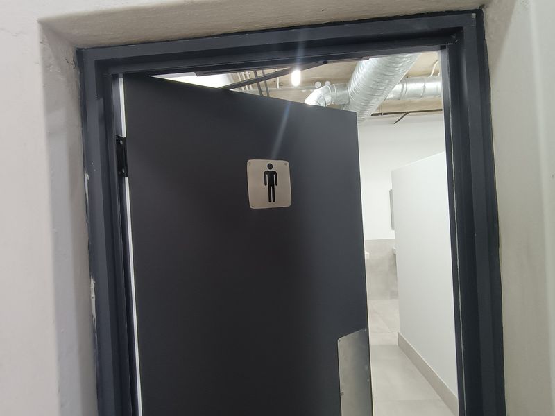 A view into a male restroom facility featuring industrial-style exposed ductwork and modern tiled flooring.